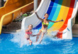 Two children on water slide at aquapark show thumb up. Summer swimming holiday. There are two water slides in aqua park. Swimming outdoor.