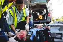 Emergency Medical Technicians Healing Injured Man On Road