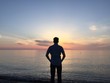 © romankosolapov - Young thoughtful man standing at the beach looking to the sunset or sunrise and dreaming about the future. Rear view.