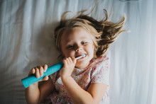 Young Girl, Lying On Bed, Brush Teeth With Electric Toothbrush