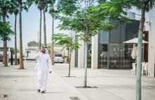 Man Wearing Traditional Middle Eastern Clothing Walking Along Street Talking On Smartphone, Dubai, United Arab Emirates
