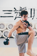 Man In Gym Wearing Boxing Gloves In Kickboxing Stance Looking At Camera