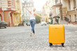 
Orange suitcase on the road in city and young woman on the background. Summer vacation and travel concept
