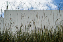 Grass In The Background Concrete Fence With Barbed Wire And Sky Clouds