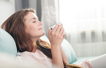 young woman sitting on couch at home and drinking coffee. casual style indoor shoot