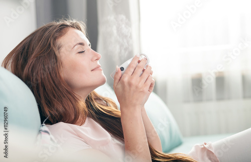 Zdjęcie XXL Młoda kobieta siedzi na kanapie w domu i picia kawy. Strzelający w stylu casual
