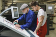 © fStop - Young worker looking at mature colleague doing quality check of printout with scanner