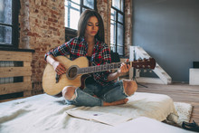 Young Woman Playing Guitar While Sitting On Bed At Home