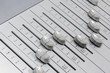 side view closeup of chrome slider buttons forming a wave pattern with small amplitude on metallic surface of a sound mixer