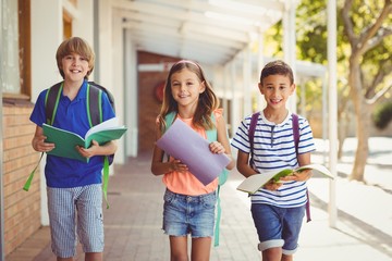 Wall Mural - Portrait of smiling school kids standing in school corridor 