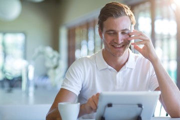 Poster - Smiling man talking on mobile phone while using digital tablet