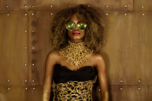 Beautiful African Woman Posing In Fashionable Sunglasses And Gold Necklace On Bronze Background