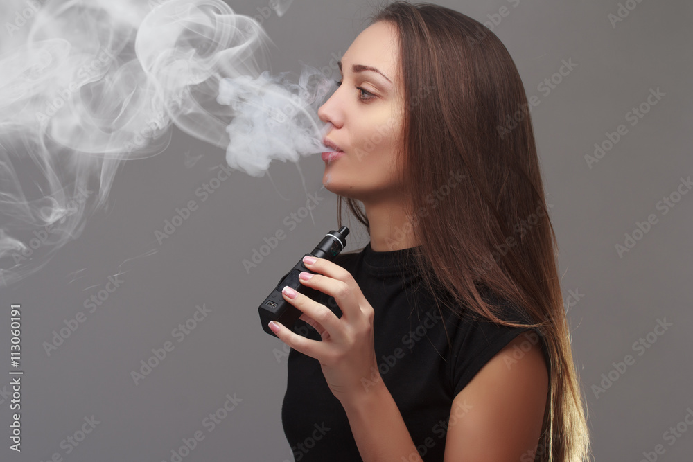 Photo Stock Young beautiful woman smoking ( vaping ) e-cigarette with smoke  | Adobe Stock