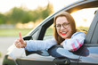 © vladstar - Young happy woman sitting in a car with thumb up