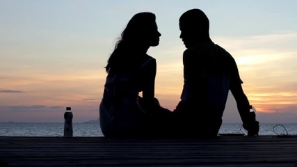 Wall Mural - Young couple sitting on the pier at sunset background
