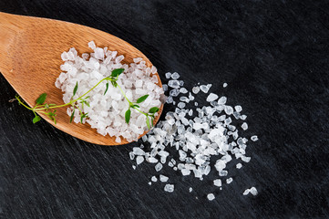 Sea salt on a wooden spoon over black slate background, selective focus, close up