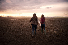 Two Girlfriends Walking Through Field At Sunrise