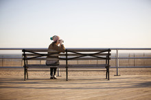 Young Woman Photographing From Boardwalk Bench