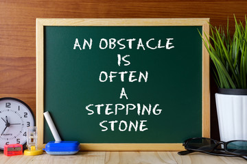 Word quote AN OBSTACLE IS OFTEN A STEPPING STONE written on green chalk board on wooden table.