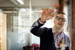 © Cavan Images - Man writing plan on glass in office