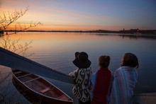 Rear View Of Friends Looking At Lake By Moored Boat During Sunset In Winter