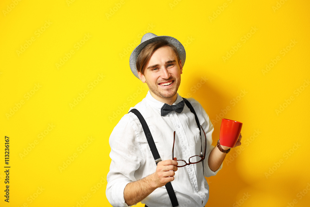 Young handsome man with a cup of coffee on bright yellow background