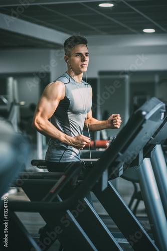 Fotografering Young man in sportswear running on treadmill at gym