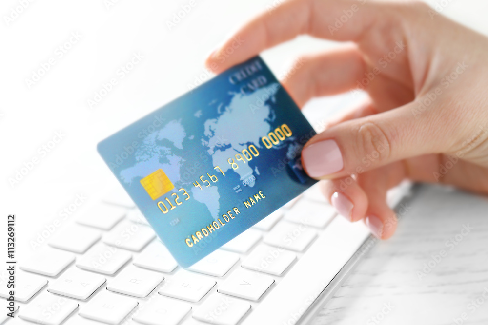 Woman hand holding credit card under keyboard, closeup