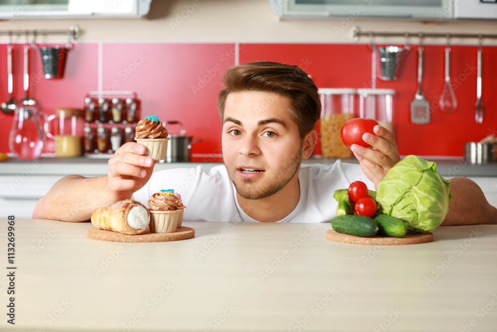 Man with healthy and unhealthy food in kitchen