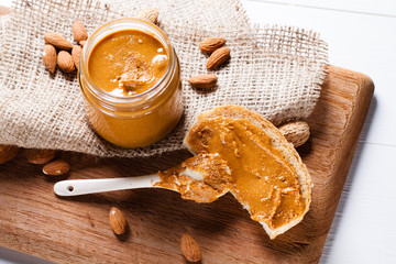 Homemade almond butter in a glass jar and sandwich smeared with a ceramic spoon.