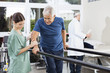 Physiotherapist Standing By Patient Walking Between Parallel Bar