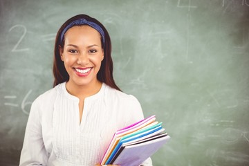 portrait of smiling school teacher holding books in classroom