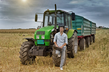 Farmer with laptop leaning on tractor