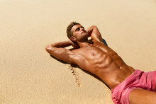 Man Body On Beach In Summer. Handsome Sexy Fit Male With Healthy Skin Sun Tan Tanning At Luxury Relax Spa Resort. Beautiful Fitness Model Relaxing, Sunbathing Lying On Sand. Summertime Travel Vacation