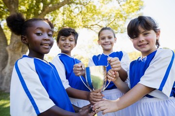 Happy children soccer team holding cup 