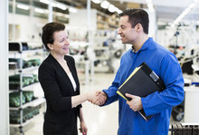 Mature Male Engineer Shaking Hands With Female Client In Factory
