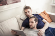 © Maskot - Young homosexual using digital tablet together while relaxing on sofa at home