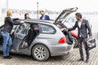 © Maskot - Colleagues discussing while businessman unloading bags from car