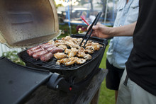 Midsection Of Men Grilling Meat On Barbecue In Yard