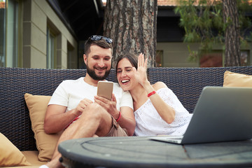 Wall Mural - Young smiling couple is conducting video call on cozy open terra