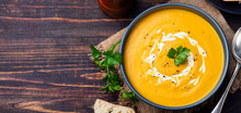 Pumpkin And Carrot Soup With Cream And Parsley On Dark Wooden Background Top View Copy Space