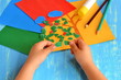 Child tearing colored paper into pieces. Home activity to improve fine motor skill development. Baby play. How to work with paper and glue. Color paper sheets, glue stick, pencils. Blue background