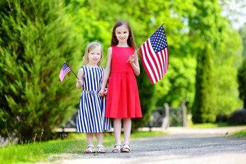 Two adorable little sisters holding american flags outdoors on beautiful summer day