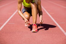 Female Athlete Tying Her Shoe Laces On Running Track