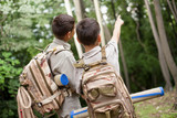 Fototapeta  - two boys go hiking with backpacks on a forest road bright sunny