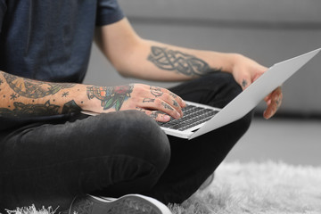 Canvas Print - Young man with tattoo using laptop on a floor at home