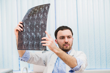 Closeup portrait of intellectual man healthcare personnel with white labcoat, looking at brain x-ray radiographic image, ct scan, mri, clinic office background. Radiology department