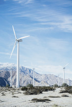 Wind Turbines On Farm By Rocky Mountain Against Sky