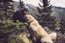 Happy Male Hiker Looking At Dog While Sitting On Mountain