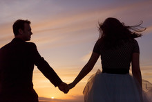 Rear View Of Couple Holding Hands Against Sky During Sunset